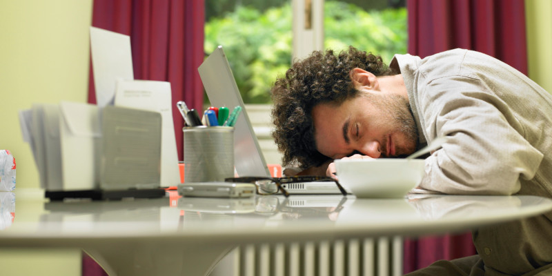 Man at breakfast table asleep on laptop computer, side view