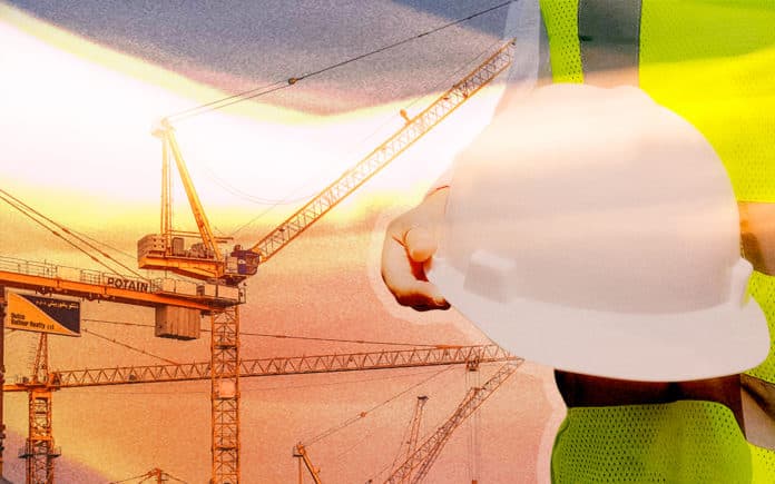 IoT Applications in Construction Someone holding a construction hat with cranes in the background